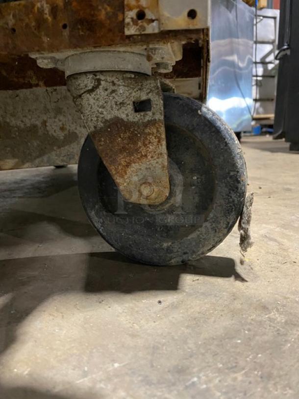 Rusty industrial caster wheel, showing wear and corrosion, attached to machinery. Suitable for repair or parts use.