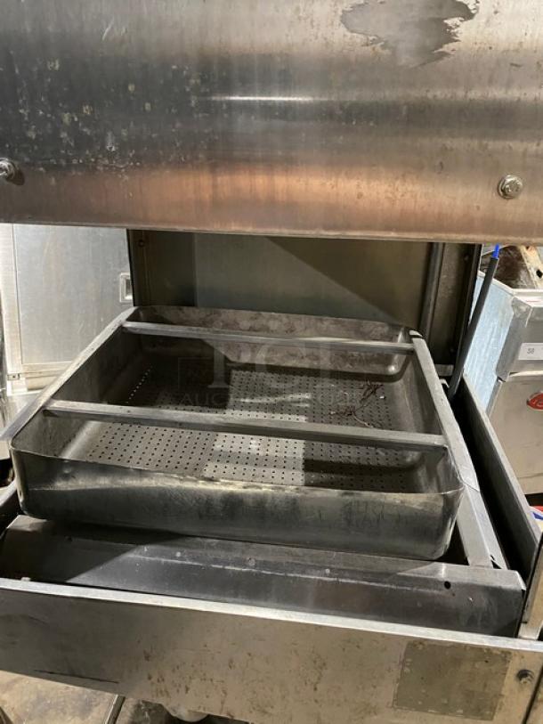 Industrial stainless steel perforated tray in used condition, housed in a metal machine. Some surface wear visible.