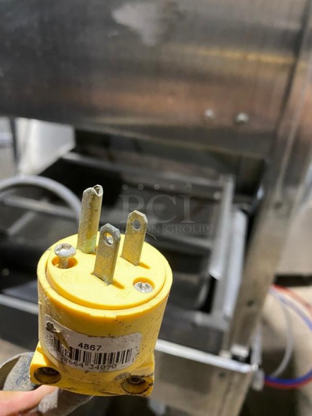 Yellow industrial power plug with three metal prongs, visible wear; barcode label reads "4867." Ideal for heavy machinery.