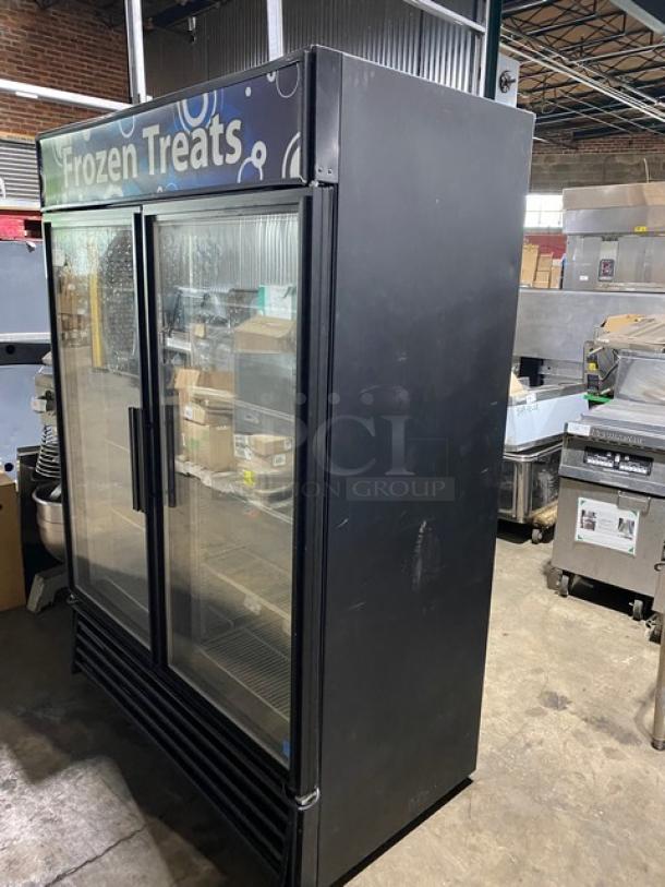 Commercial double-door freezer with "Frozen Treats" sign. Black exterior, glass doors. Visible scratches, good condition.