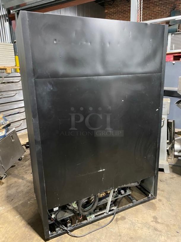 Black industrial refrigerator unit, large vertical design, showing back panel with exposed wiring. Moderate wear, some dents.