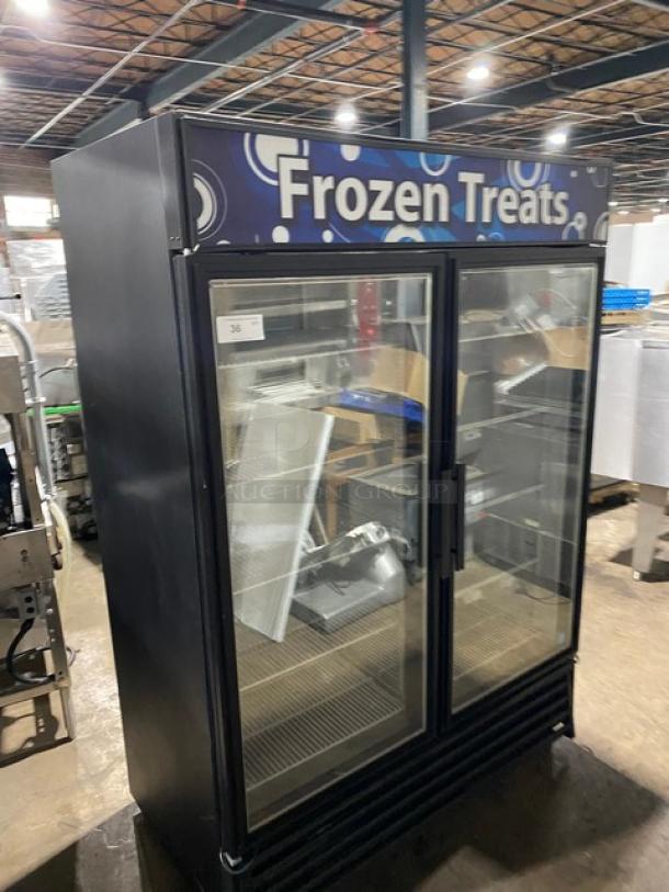 Commercial double-door freezer labeled "Frozen Treats," glass doors, black frame, metal shelving, used condition.