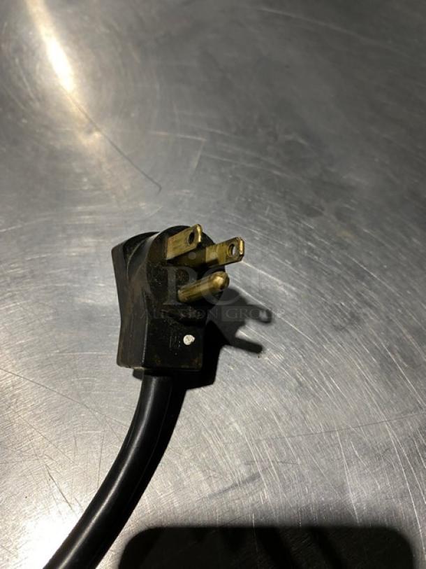 Black three-prong electrical plug with visible slight wear, suitable for heavy-duty appliances, on a reflective surface.