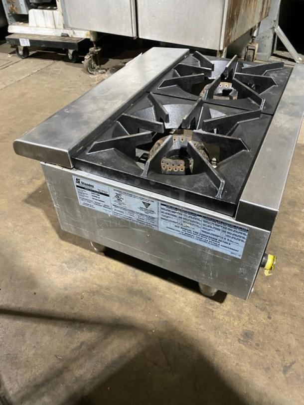 Stainless steel four-burner gas stove with cast iron grates, industrial model. Manufacturer labels detail specs and safety info.