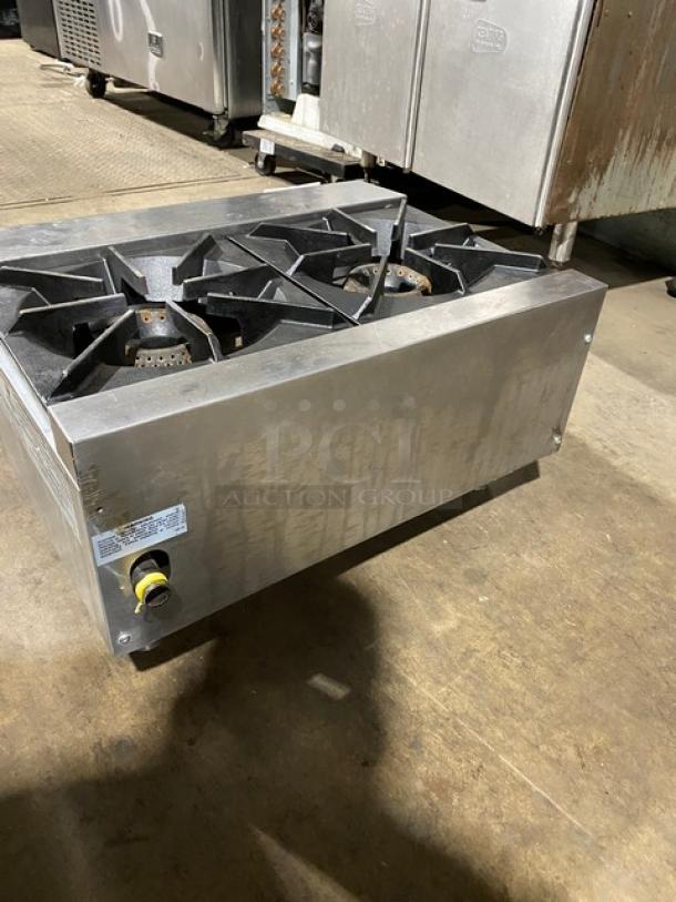 Commercial stainless steel gas stovetop, four burners, signs of wear, visible control knob, manufacturer's label on the side.