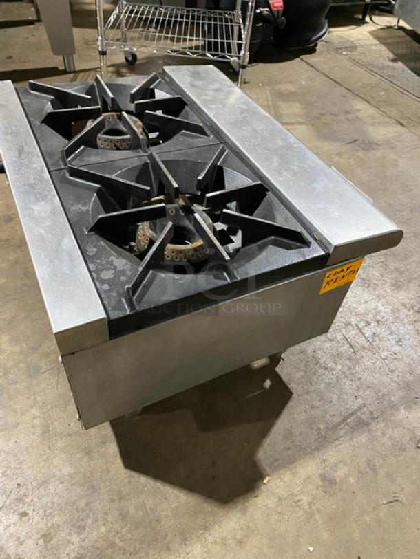 Commercial double-burner gas stove in used condition. Features heavy-duty cast iron grates, stainless steel body. Tag: "Parts Needed."