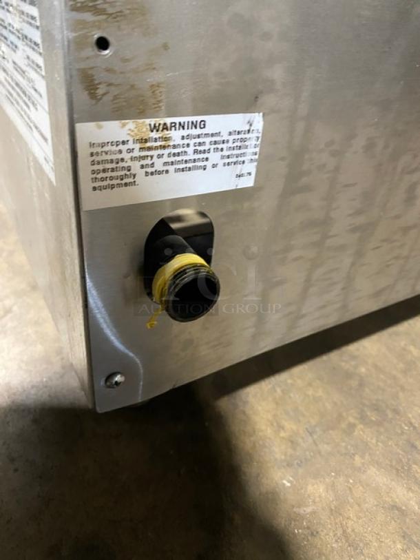 Metal appliance with visible warning label and threaded nozzle. Warning advises proper installation. Item shows signs of wear.