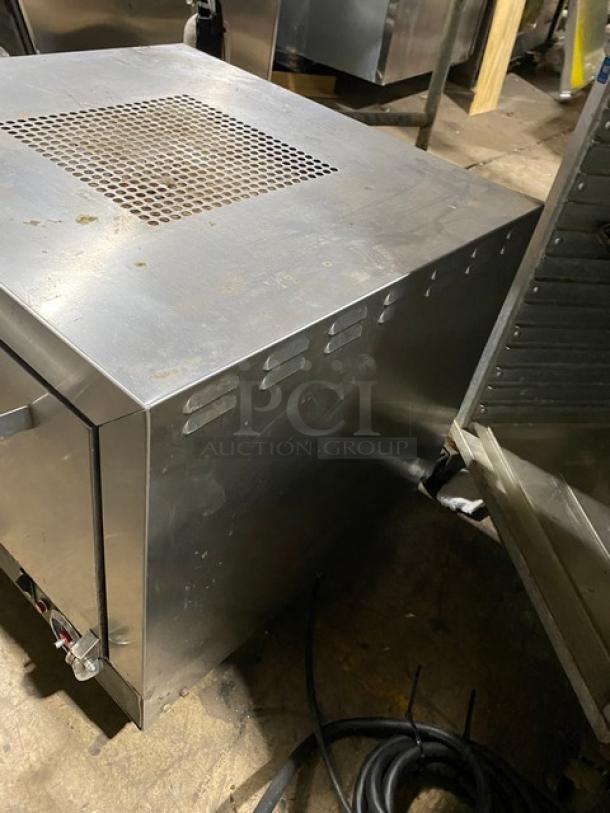Industrial stainless steel appliance with ventilation slots, used condition. Features include top grate and side handle. Cables visible.