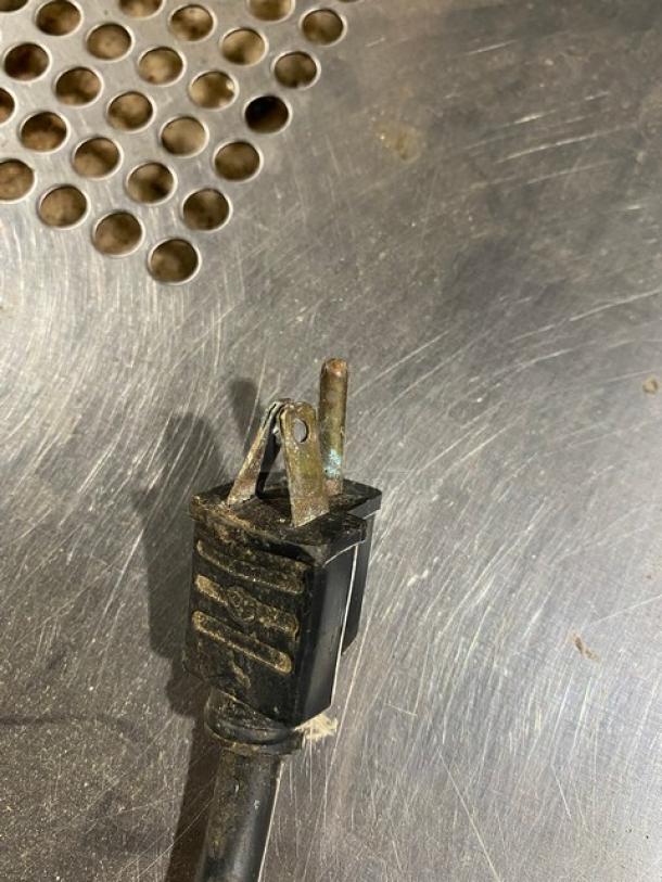 Worn black electrical plug on a scratched metal surface, showing signs of rust and wear; no visible markings.