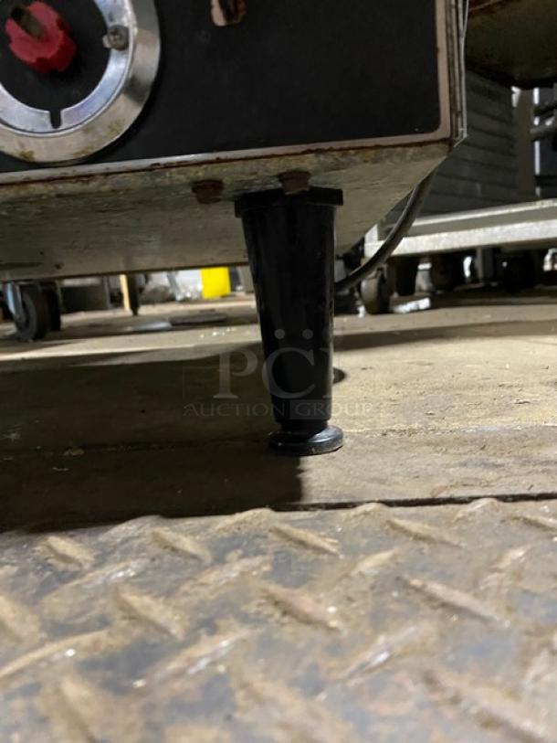 Heavy-duty equipment with adjustable metal leg, set on industrial floor; visible wear and red knob control.