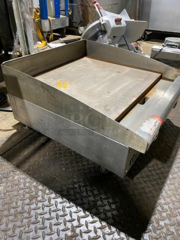 Commercial stainless steel griddle on wheels, used condition, rust on cooking surface, red safety tape on handle, indoor setting.
