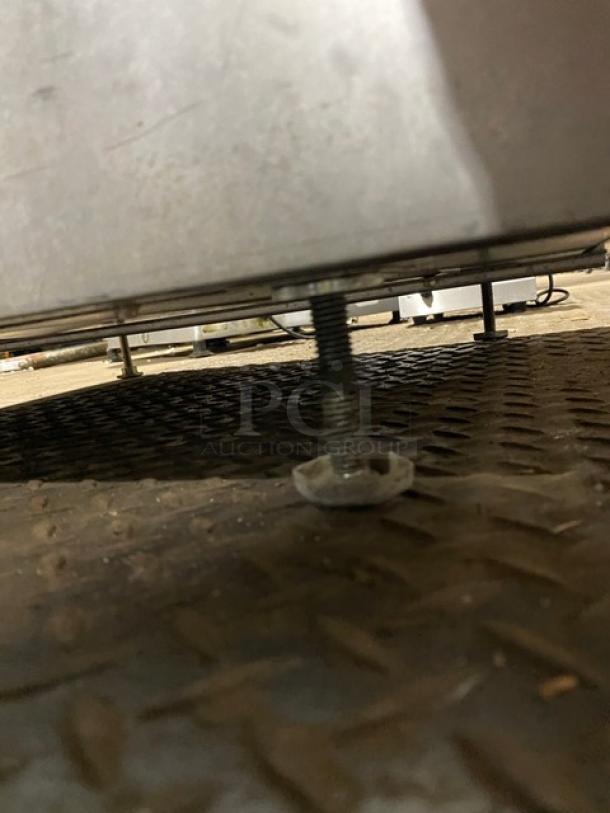 Industrial metal machinery leg with adjustable threaded foot on textured metal floor, showing wear.