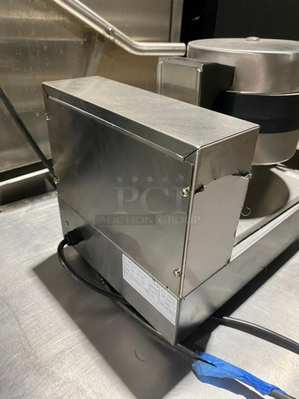 Stainless steel commercial waffle maker, clean, with visible power cord and metal casing. Features manufacturer's label.