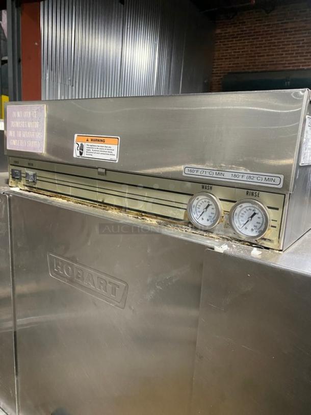 Hobart industrial dishwasher with temperature gauges, stainless steel body, visible wear, and safety warning labels.
