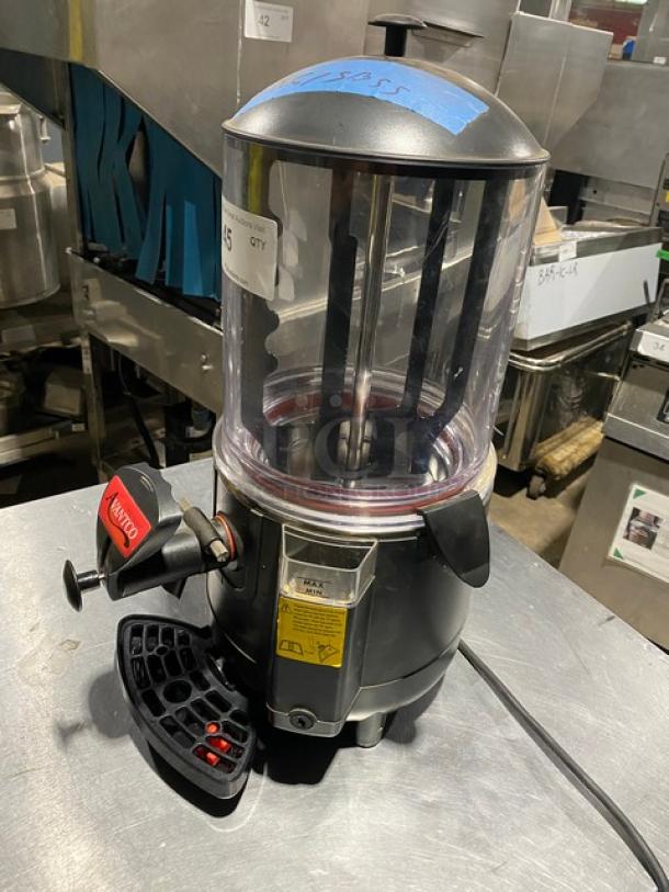 Commercial beverage dispenser with clear container, black base, and spigot. Labels indicate caution for hot liquids. Good condition.