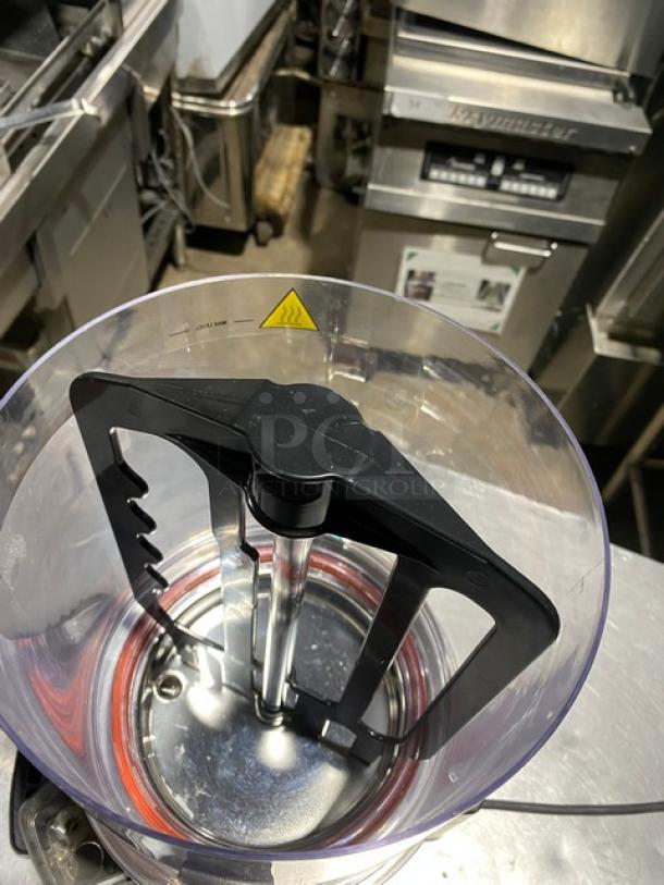 Commercial blender with stainless steel base, sturdy black blade assembly, clear container. Visible safety warning label.
