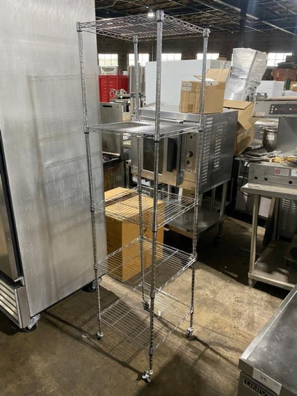 Chrome wire shelving unit with wheels, five tiers, adjustable height. Ideal for storage, in good condition. Industrial setting.