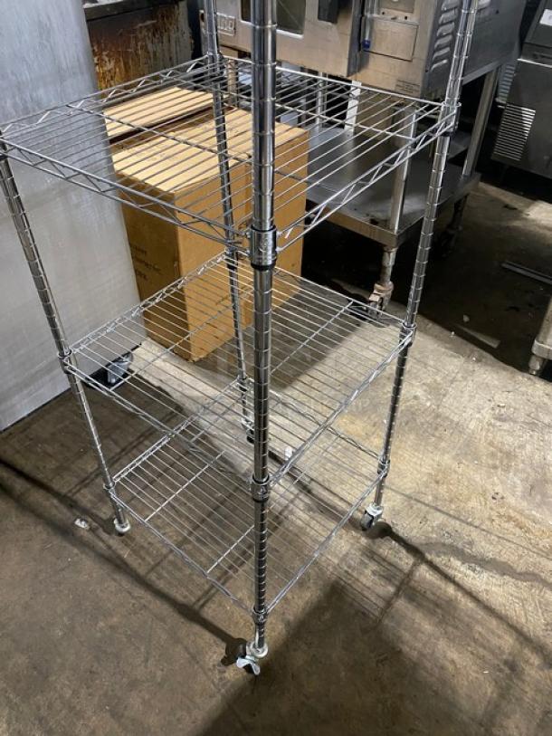 Metal wire shelving unit on wheels, four tiers, silver finish, adjustable shelves, sturdy, suitable for storage or display.