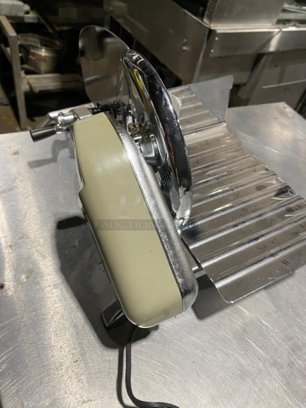 Electric meat slicer with stainless steel blade, beige motor housing, corded power, and ribbed food tray, in used condition.