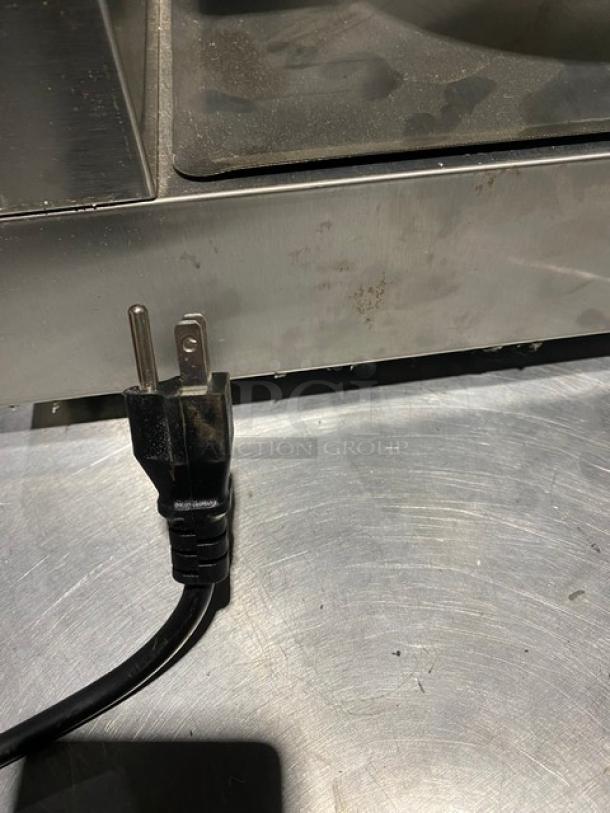 Stainless steel kitchen appliance with power cord, visible wear. Likely commercial use, needs cleaning. No visible labels.