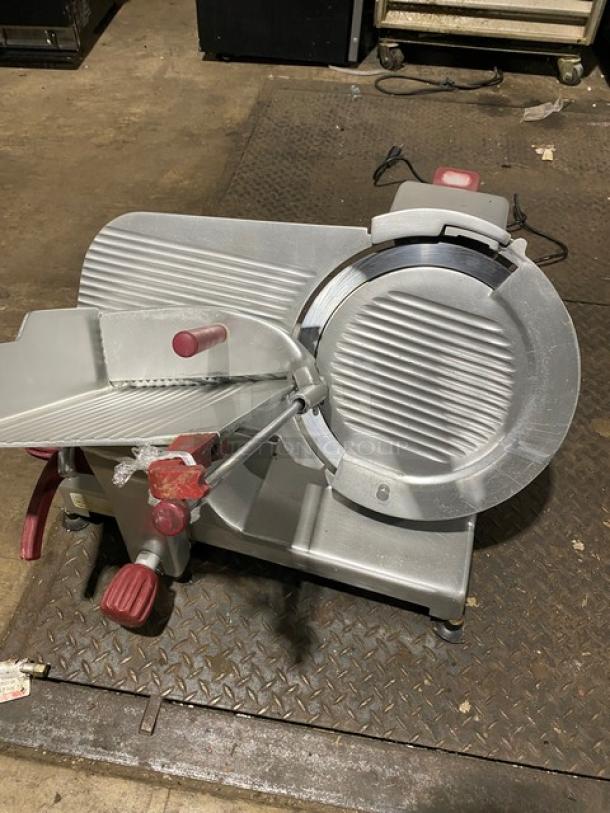 Commercial deli meat slicer with stainless steel body and red knobs. Slightly worn condition, suitable for heavy-duty use.