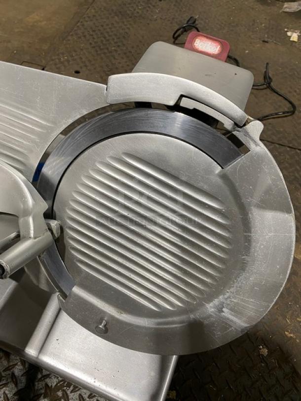 Commercial meat slicer with serrated blade and stainless steel construction. Visible wear, suitable for high-volume kitchens.