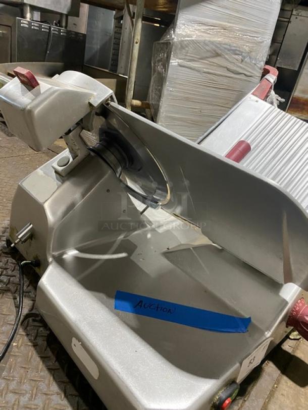 Industrial meat slicer with a metal body and blade, labeled "Auction" in blue tape, in used condition.