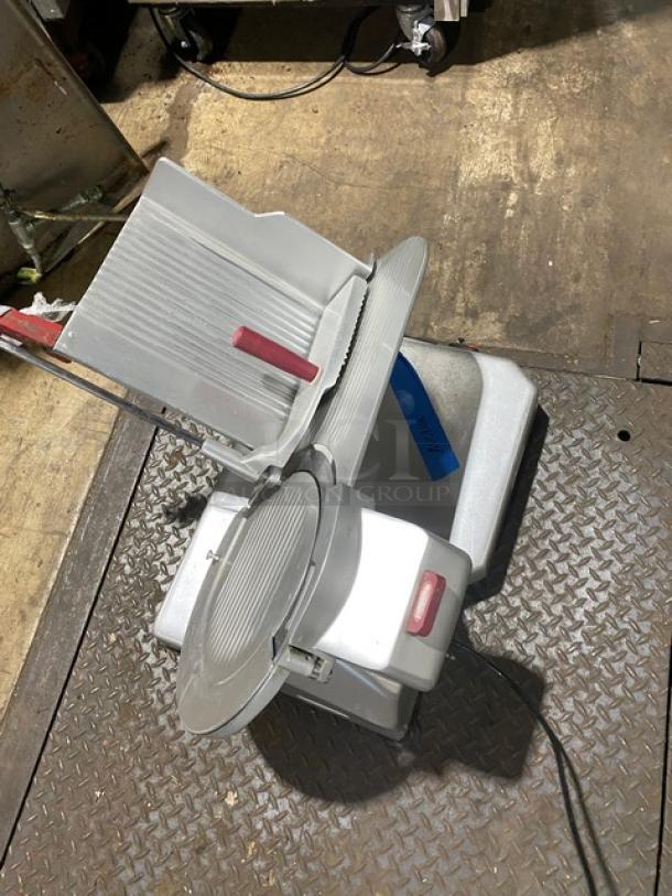 Commercial meat slicer in used condition, featuring an adjustable blade, red handle, and power cord. Metal body shows wear.