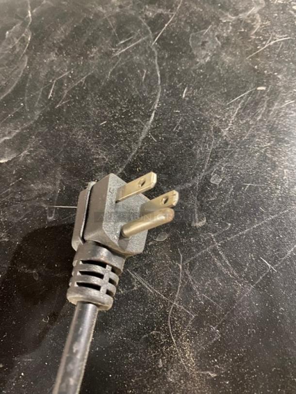 Three-prong power cord plug on black surface, showing slight wear. Suitable for electrical appliances.
