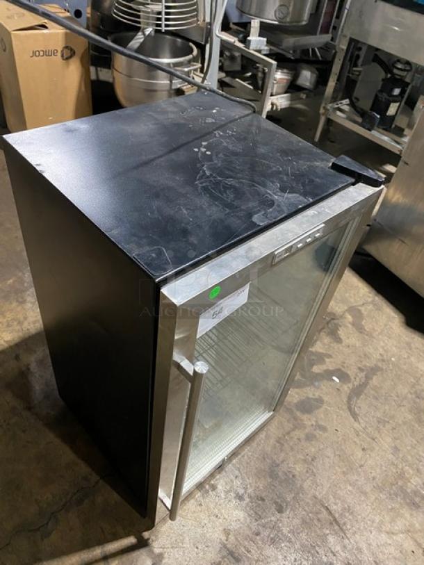 Commercial mini fridge with glass door, stainless steel frame, and interior shelving. Minor surface wear visible. Marked "54".