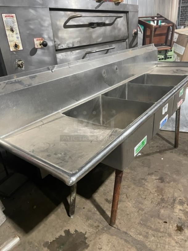 Commercial stainless steel 3-compartment dishwashing sink with left and right drain boards, backsplash, on sturdy legs.