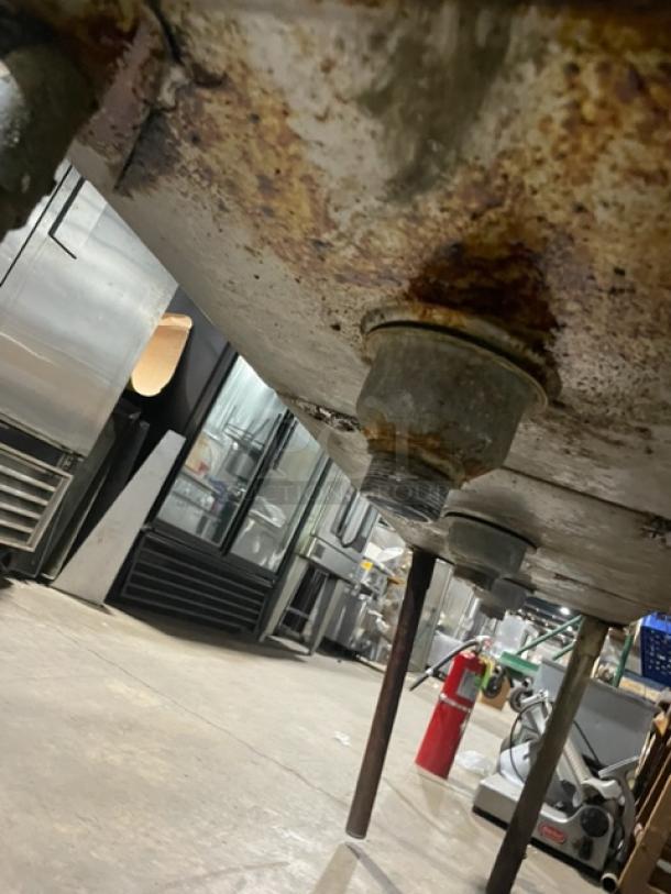 Commercial stainless steel 3-compartment sink underside, visible rust and drainage pipes, installed on metal legs.