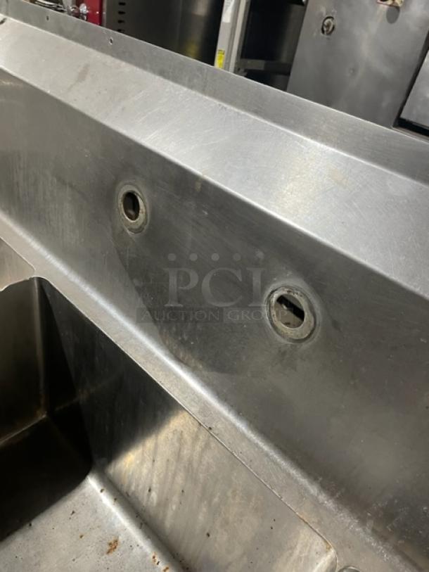 Commercial stainless steel 3-compartment sink with left and right drain boards, backsplash, on legs; visible wear, ideal for kitchen use.