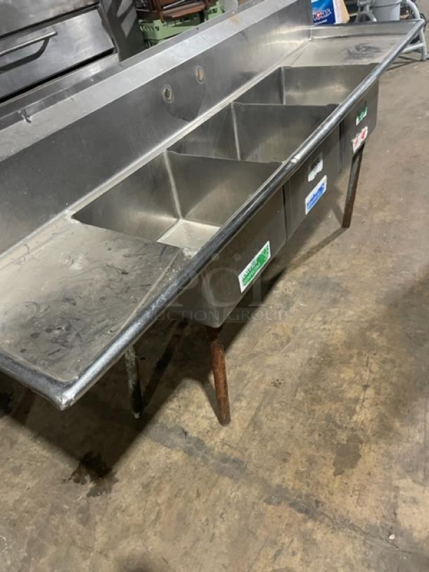 Commercial stainless steel 3-compartment sink with left/right drain boards and backsplash on legs, slightly used.
