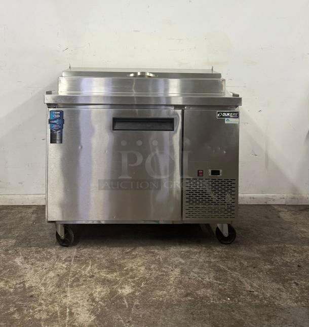 Dukers stainless steel commercial refrigerator with single door, caster wheels, and cooling vent. Includes warranty tag.