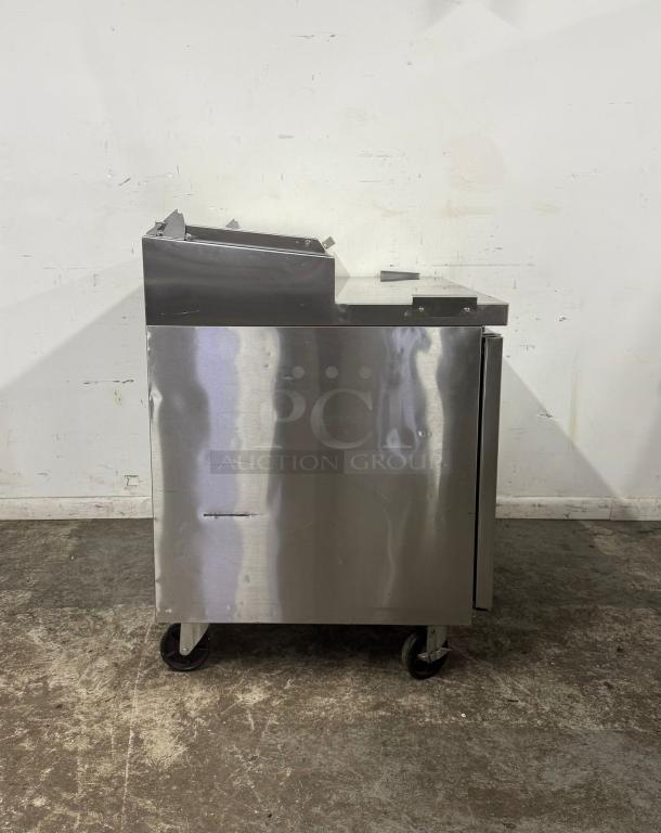 Stainless steel commercial refrigerator on wheels, used, with visible scratches. Ideal for catering or restaurant use.