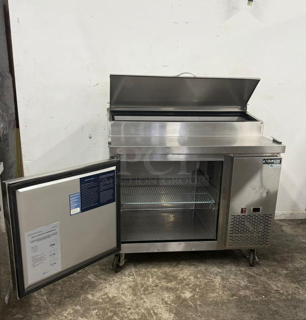 Stainless steel Dukers Commercial Refrigerator, open lid, shelves inside, instructions on door, on casters, excellent condition.