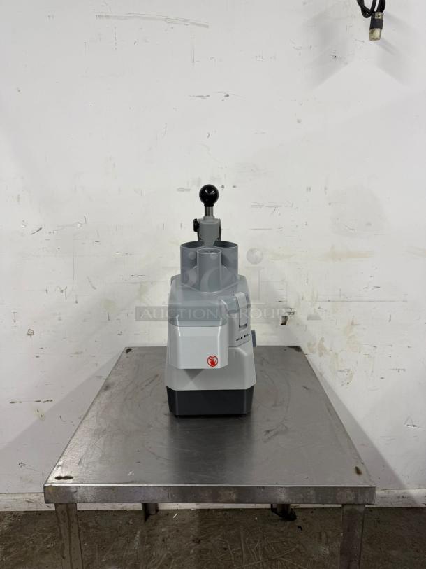 Industrial tabletop food processor with large chute, gray exterior, and red logo. Excellent condition on metal table.
