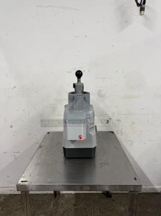 Industrial tabletop food processor with large chute, gray exterior, and red logo. Excellent condition on metal table.
