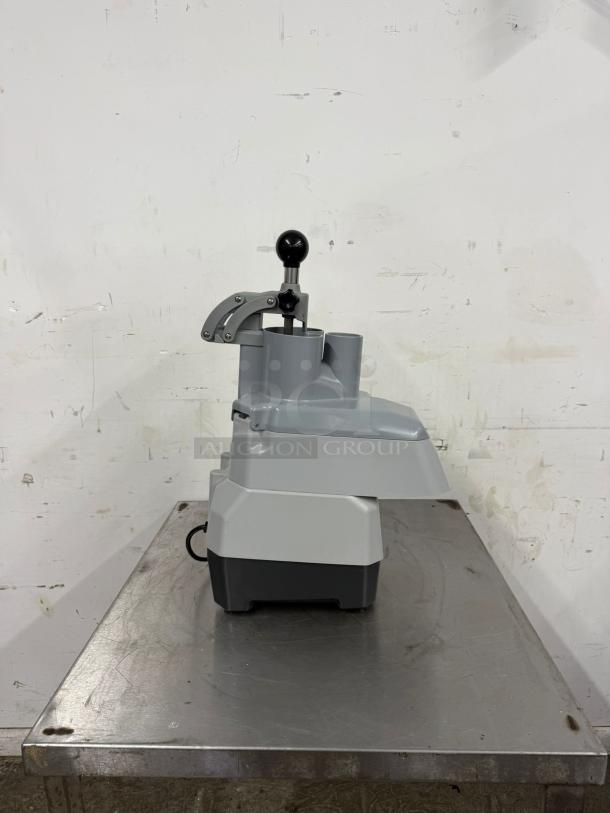 Commercial-grade food processor in excellent condition, grey and black, with a sturdy metal lever handle, shown on a metal table.
