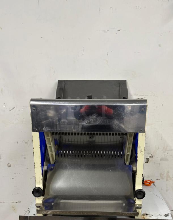 Automatic bread slicer with a stainless steel blade, used condition. Features adjustable knobs and safety guards. Suitable for bakery use.