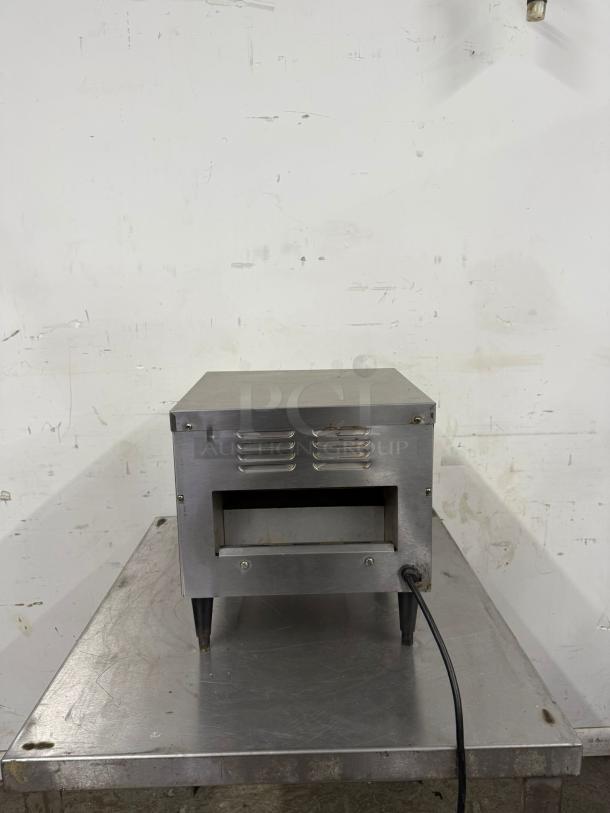 Stainless steel toaster oven with ventilation slots, black legs, electrical cord. Good condition, slight surface wear.