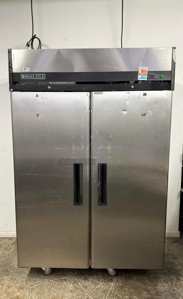 Commercial stainless steel Maxx Cold refrigerator, two-door, large capacity, visible wear, wheels attached for mobility.
