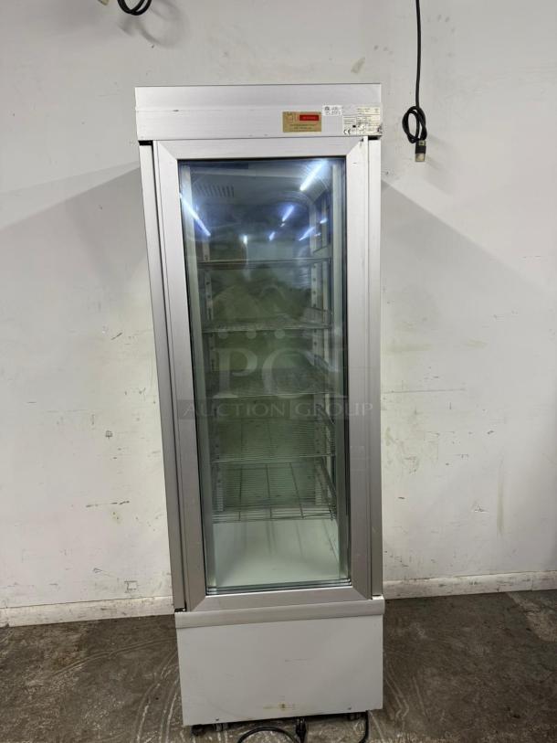 Commercial glass door refrigerator with metal shelves, silver frame, and power cord. Good condition, manufacturer's label visible.