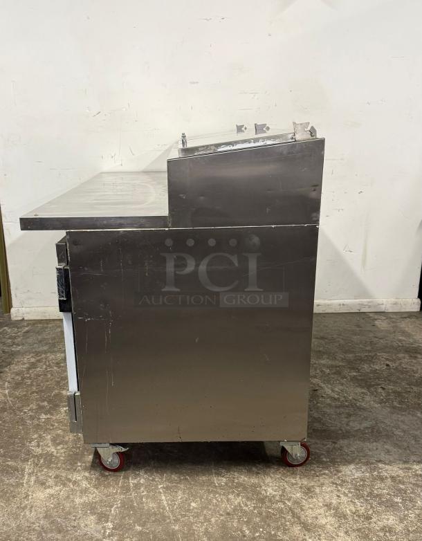 Stainless steel commercial prep table with raised backsplash, on caster wheels. Good condition, minor surface scratches.
