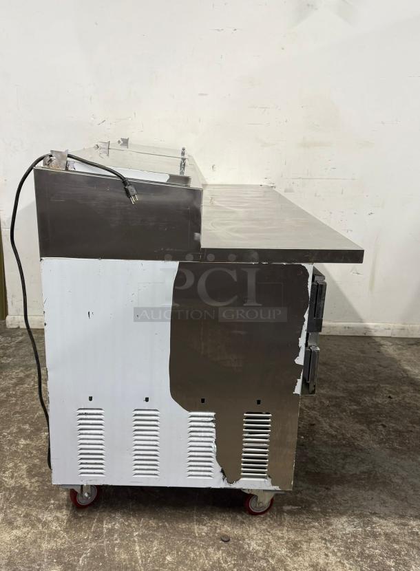 Commercial stainless steel prep table with electric cord, significant wear, chipped paint, and mounted on red caster wheels.