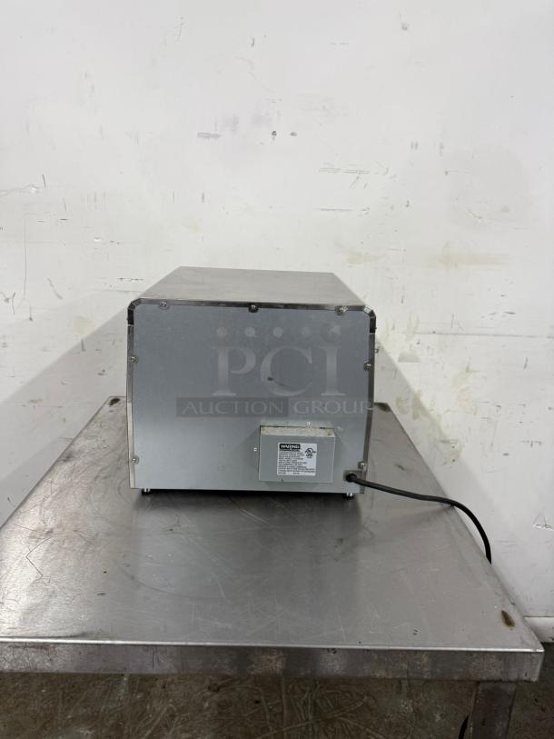Commercial kitchen appliance with a metallic finish on a stainless steel table. Wiring connected. Label shows electrical specifications. 
