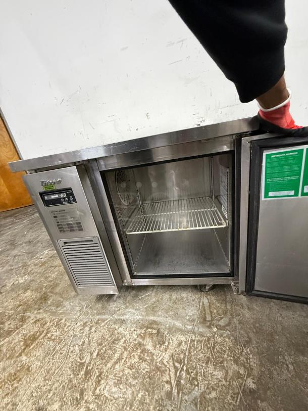 Stainless steel undercounter refrigerator, single door, visible wire shelf, digital temperature display, well-maintained.