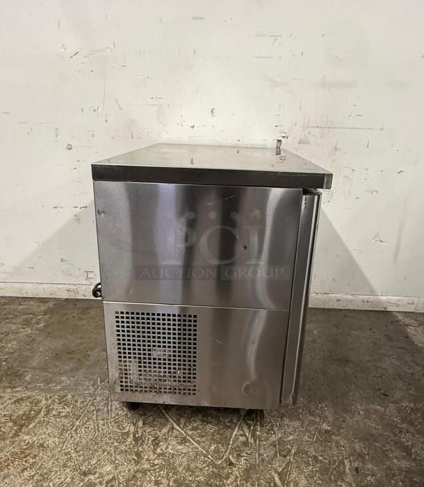 Stainless steel commercial refrigerator with single door, vent at the bottom, positioned on a concrete floor, good condition.