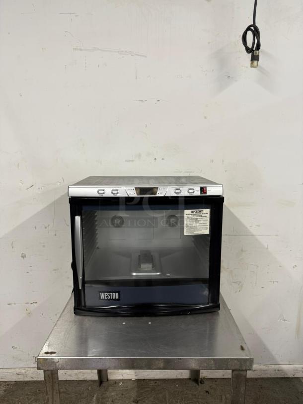 Weston countertop food warmer in good condition. Features digital controls, glass front, and visible caution label.
